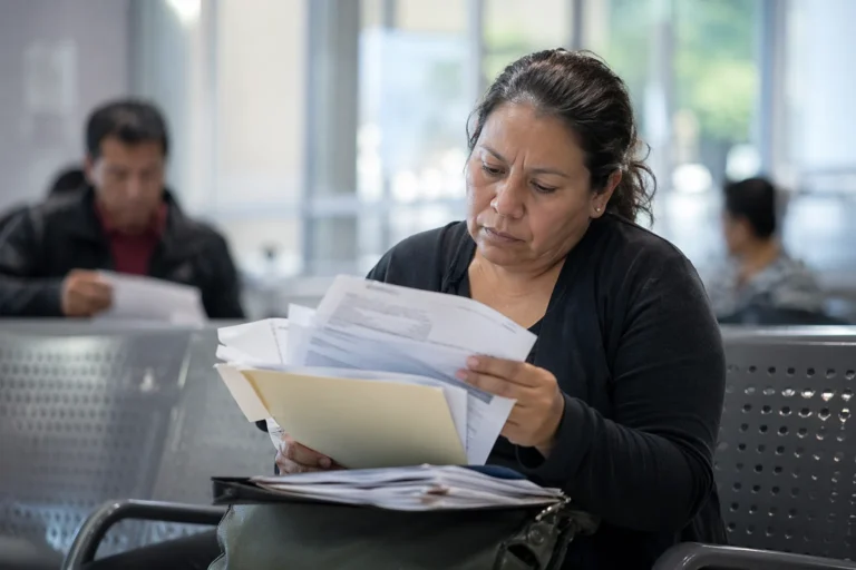 Mujer adulta mexicana revisa documentos médicos y formularios en sala de espera institucional mientras enfrenta trámites para terapias de discapacidad.
